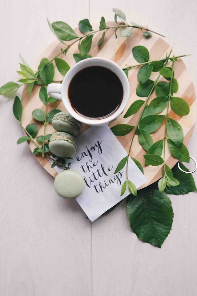 Tasse de café entourée de macarons verts et d'un message enjoy the little things