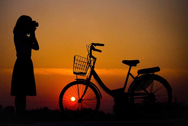 Photo d'un coucher de soleil avec un soleil rouge et au premier plan une femme debout devant son vélo