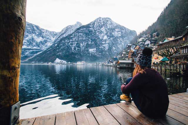 Photo d'une femme assise sur une plateforme en bois au bord d'un lac avec des montagnes en fond