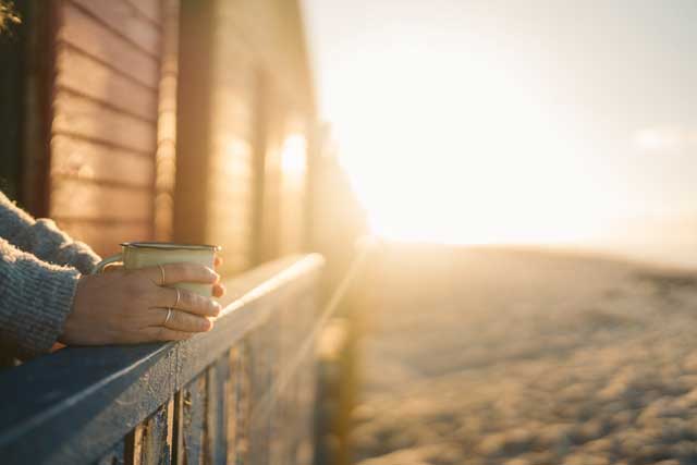 Photo faisant apparaître les mains d'une personne tenant une tasse au lever du soleil